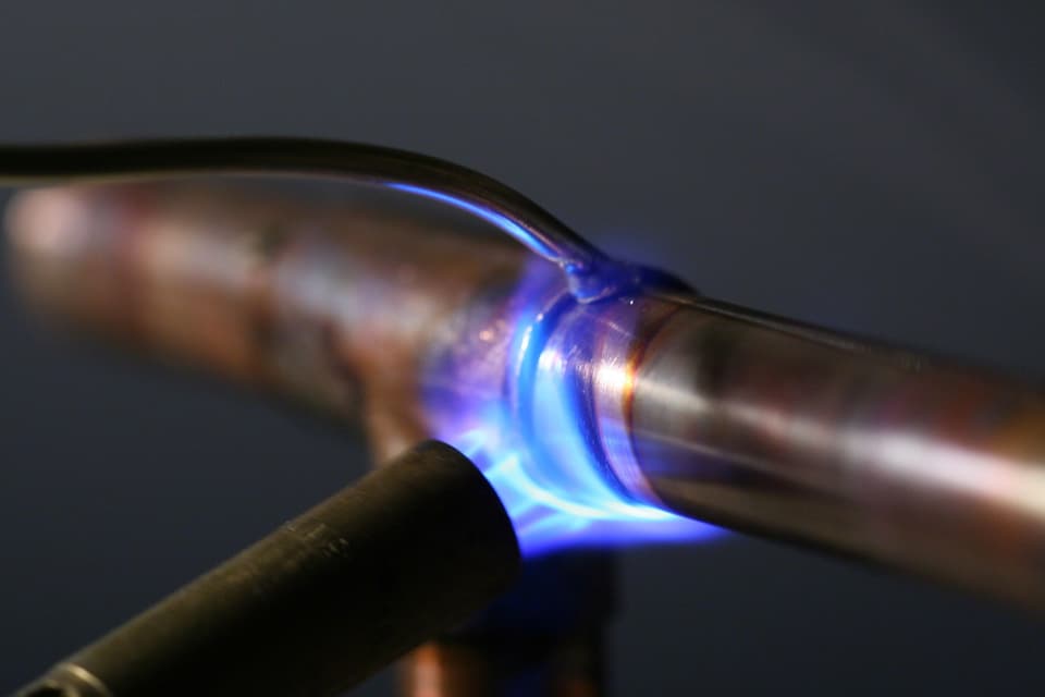 A blue torch flame on a copper pipe joint as it is soldered.