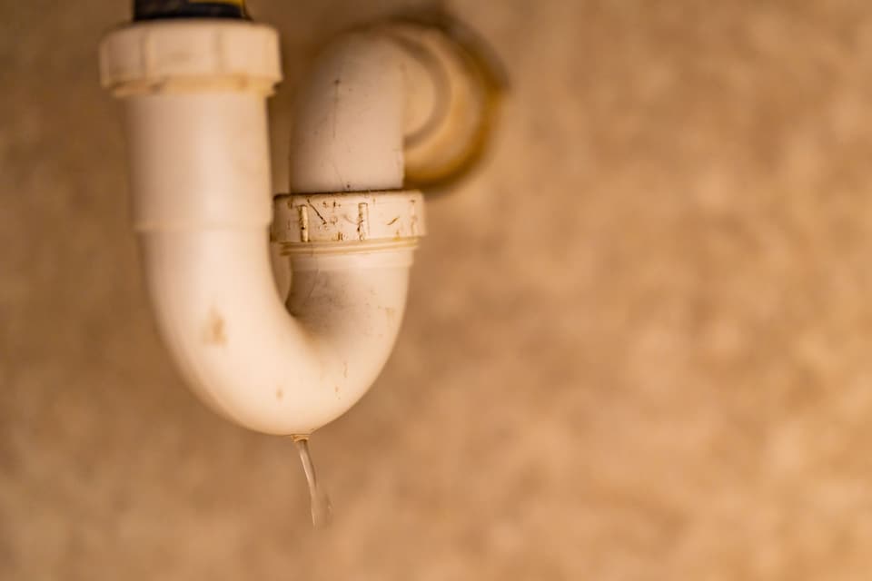 Water running from the joint of a white drain trap under a sink.