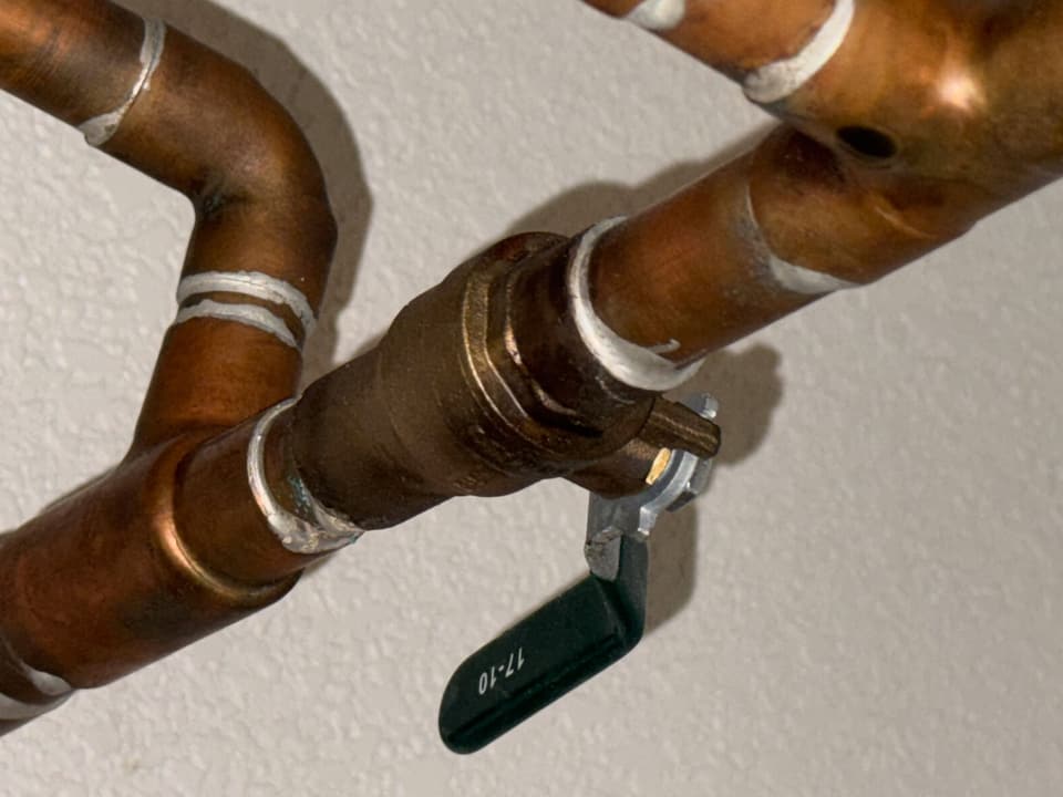Soldered copper water pipes and a brass shutoff valve against a white wall.