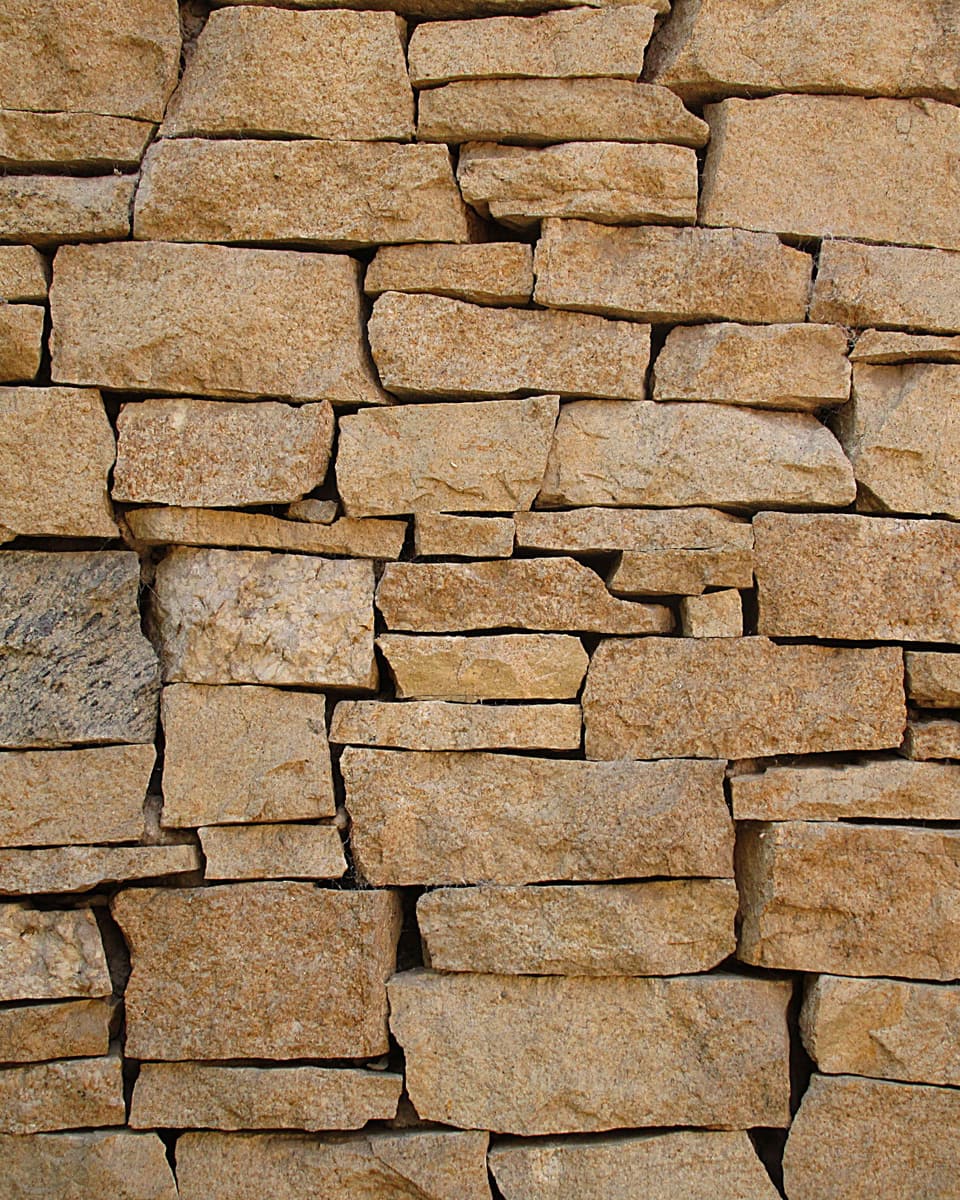 A dry-stacked wall of flat, sand-coloured stones laid in uneven courses.
